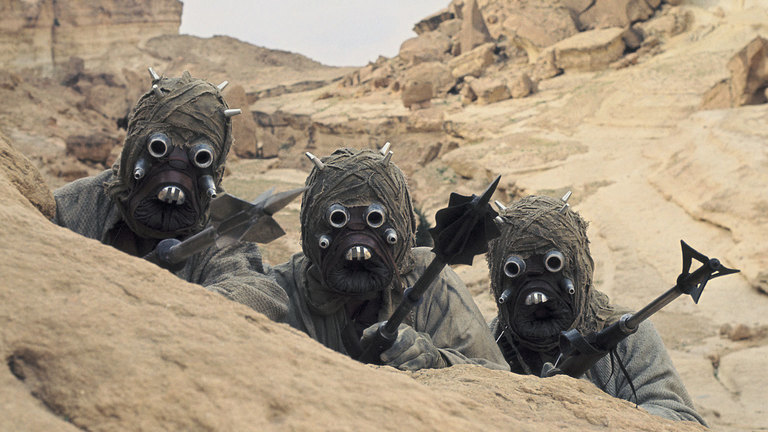 Tusken Raiders from Star Wars, wearing tan robes and yielding weapons.