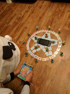 A person dressed in Animal Crossing attire, holding a copy of Animal Crossing sitting folk, praying over a pentagram made of Animal Crossing amiibo cards with a Nintendo Switch in the middle.