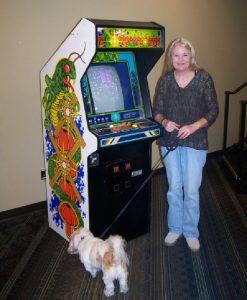 A woman in front of the "Centipede" arcade machine, with a dog on a leash.