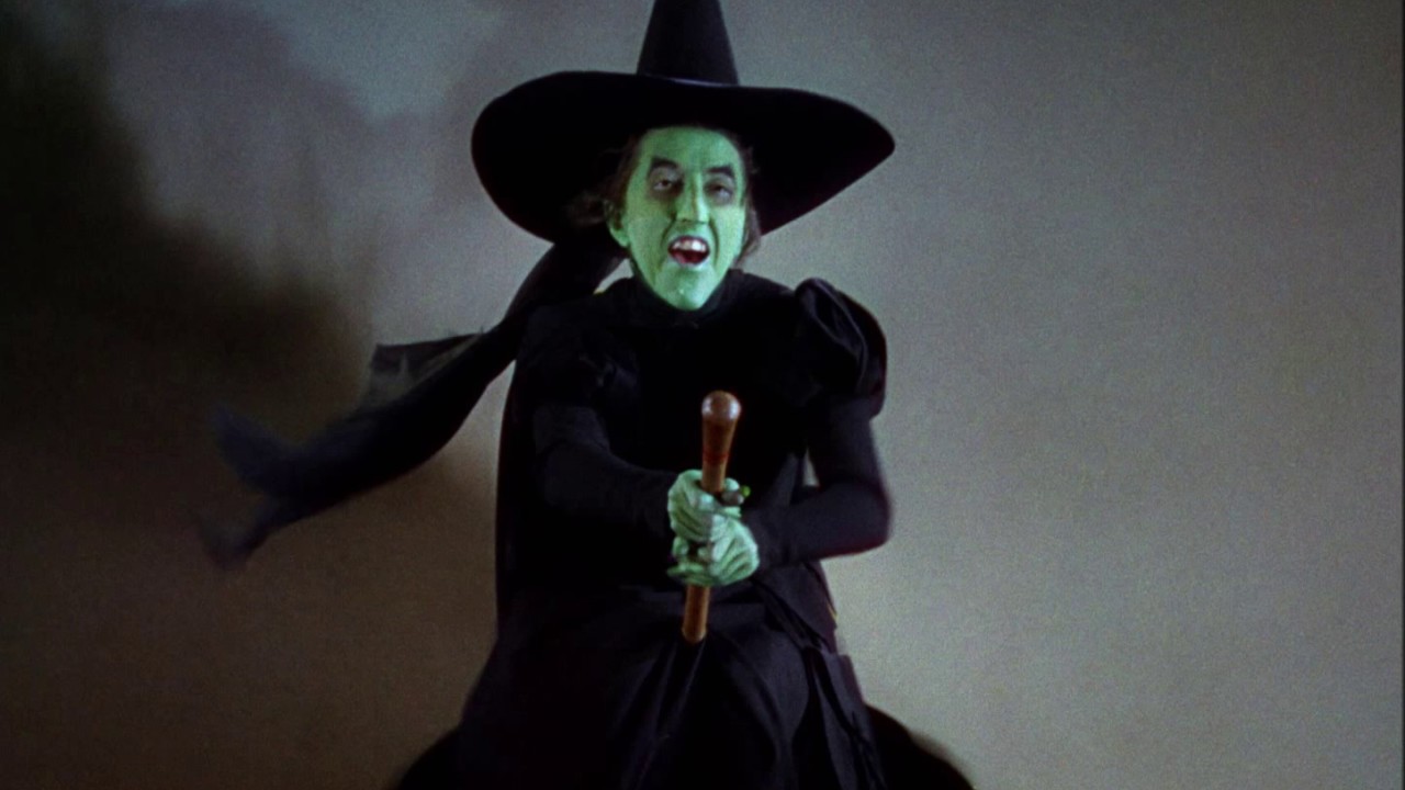 A green witch rides a broomstick