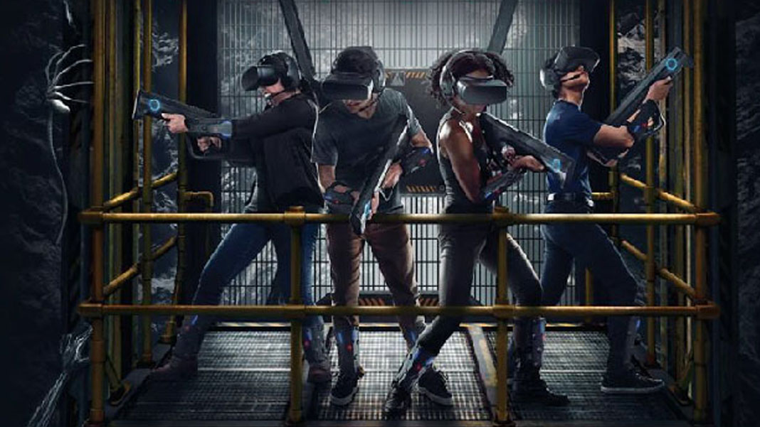 Promotional image of “Alien: Descent.” It shows four people wearing VR gear (visor headset, plastic gun, lightweight devices on their arms and legs) on a yellow metal lift, with facehugger aliens crawling around.